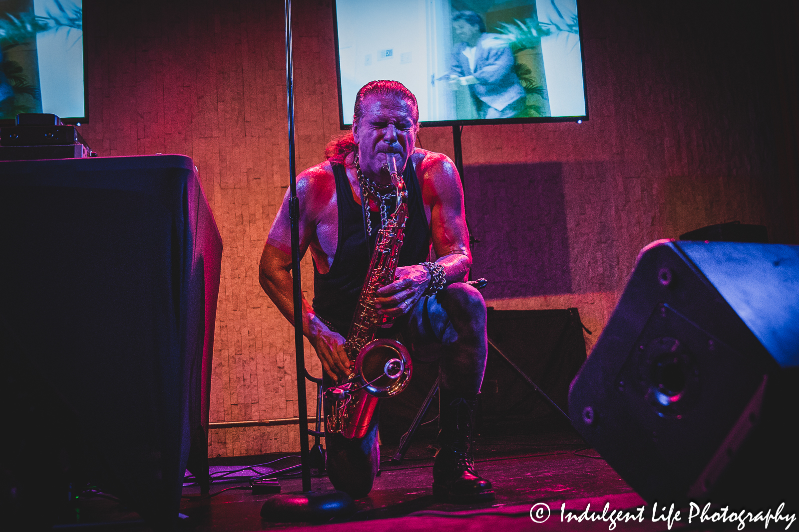 Tim Cappello playing the saxophone on one knee with a "Miami Vice" clip in the background at the recordBar in Kansas City, MO on June 15, 2023.